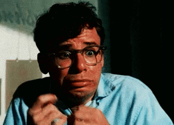 A Man With Glasses And A Blue Shirt Is Making A Scared Face . GIF
