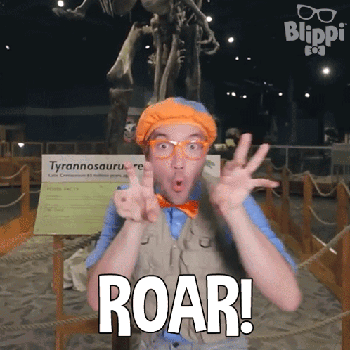 A Man With Glasses And A Bow Tie Says Roar In Front Of A Dinosaur Skeleton GIF