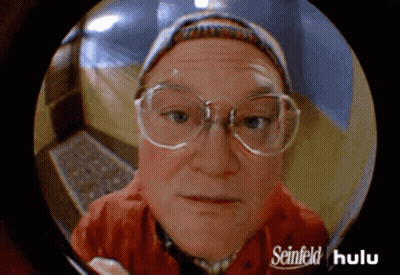 A Man With Glasses And A Hat Is Looking Through A Peephole With Seinfeld Hulu Written On It GIF