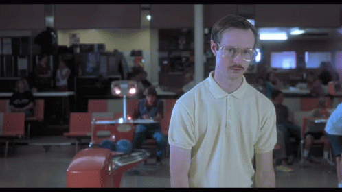 A Man With Glasses And A Moustache Stands In A Bowling Alley GIF