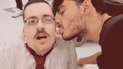 A Man With Glasses And A Mustache Is Kissing Another Man On The Cheek GIF