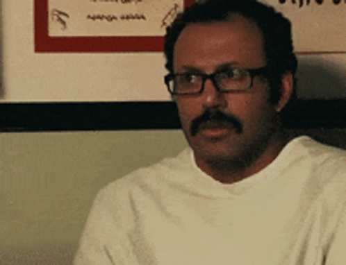 Man With Glasses And Mustache Sitting In Front Of Sign GIF