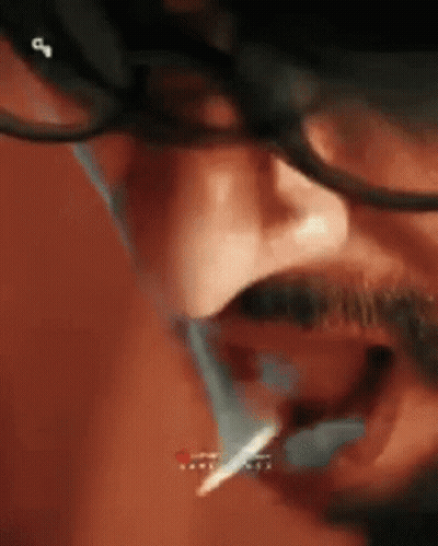 A Man With Glasses And A Mustache Is Smoking A Cigarette With A Lighter In His Mouth . GIF