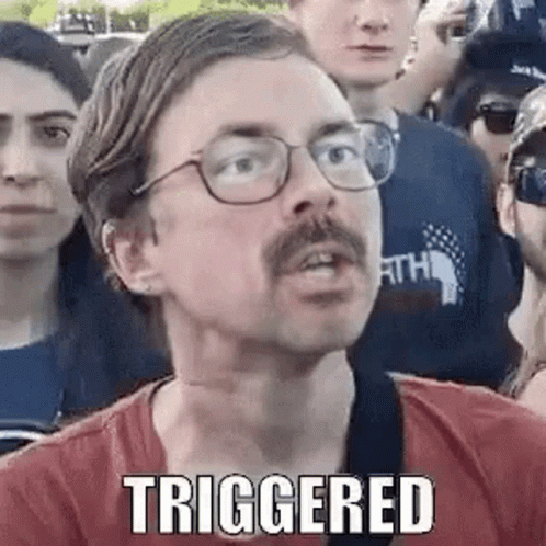 A Man With Glasses And A Mustache Is Standing In A Crowd Of People And Making A Funny Face . GIF
