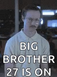 A Man With Glasses And A Mustache Is Standing In Front Of A Sign That Says Big Brother 27 Is On . GIF