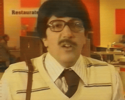 A Man With Glasses And A Mustache Is Standing In Front Of A Sign That Says Restaurante GIF
