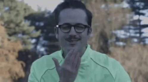 A Man With Glasses And A Mustache Is Wearing A Green Jacket And Making A Face . GIF