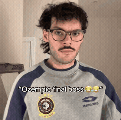 A Man With Glasses And A Mustache Is Wearing A Sweatshirt That Says Ozempic Final Boss GIF