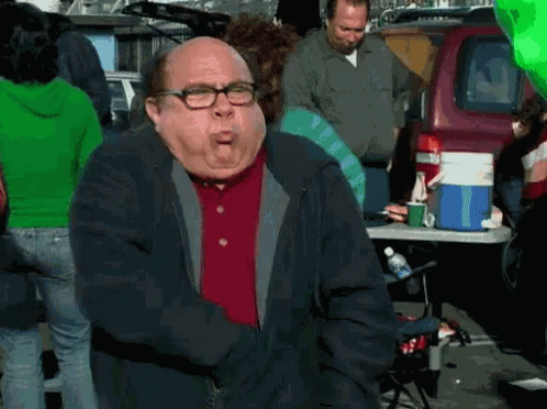 A Man With Glasses And A Red Shirt Is Standing In Front Of A Table With A Cooler On It . GIF