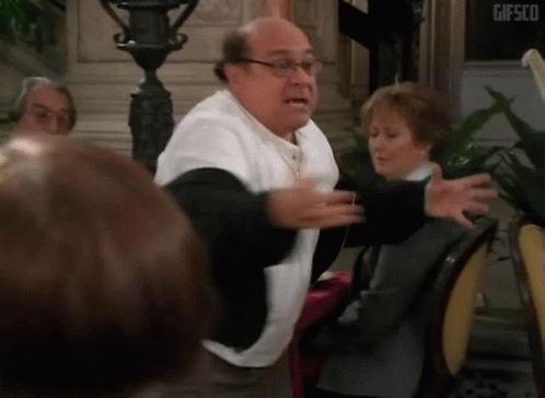 A Man With Glasses And A White Shirt Is Standing In Front Of A Group Of People GIF