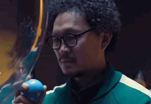 A Man With Glasses Holds A Blue Ball In His Hand GIF