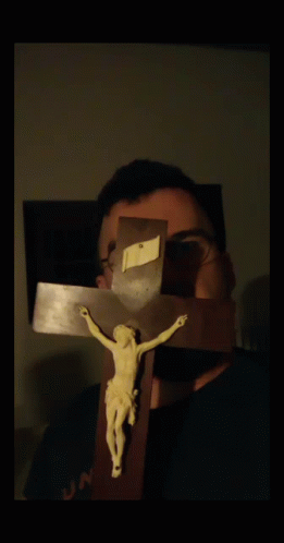 A Man With Glasses Holds A Crucifix In Front Of His Face GIF