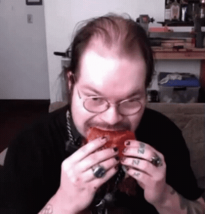 A Man With Glasses Is Eating A Piece Of Meat . GIF