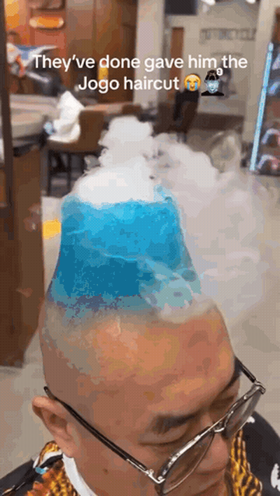 A Man With Glasses Is Getting A Haircut That Looks Like A Mountain With Smoke Coming Out Of It . GIF