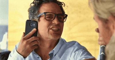 A Man With Glasses Is Holding A Cell Phone To His Ear GIF