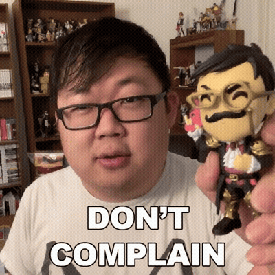 A Man With Glasses Is Holding A Figurine That Says " Do N't Complain " On It GIF