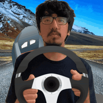 A Man With Glasses Is Holding A Steering Wheel In Front Of A Mountain GIF