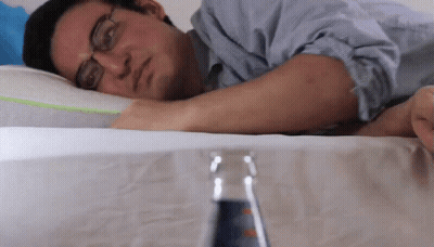 A Man With Glasses Is Laying On A Bed With A Bottle Of Soda In Front Of Him GIF