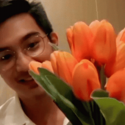 A Man With Glasses Is Looking At A Bouquet Of Orange Flowers GIF