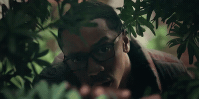A Man With Glasses Is Peeking Out From Behind A Tree GIF
