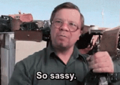 A Man With Glasses Is Saying So Sassy While Holding A Gun GIF