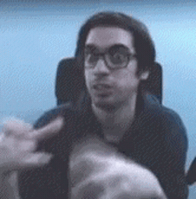 A Man With Glasses Is Sitting In A Chair And Pointing At Something GIF