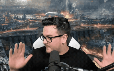 A Man With Glasses Is Sitting In Front Of A Microphone With His Hands Outstretched GIF