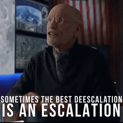A Man With Glasses Is Sitting In Front Of A Sign That Says Sometimes The Best Deescalation Is An Escalation GIF