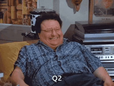 A Man With Glasses Is Sitting On A Couch And Laughing With The Word Q2 On His Face GIF