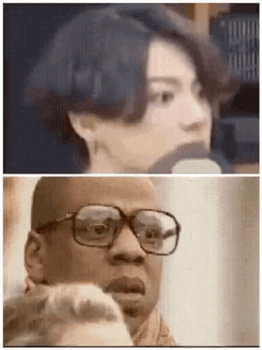A Man With Glasses Is Talking Into A Microphone Next To A Woman . GIF