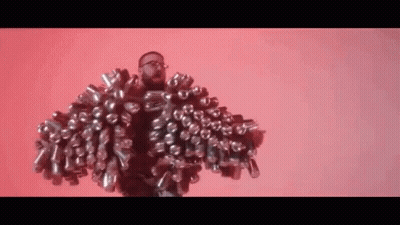 A Man With Glasses Is Wearing A Jacket Made Out Of Cans . GIF