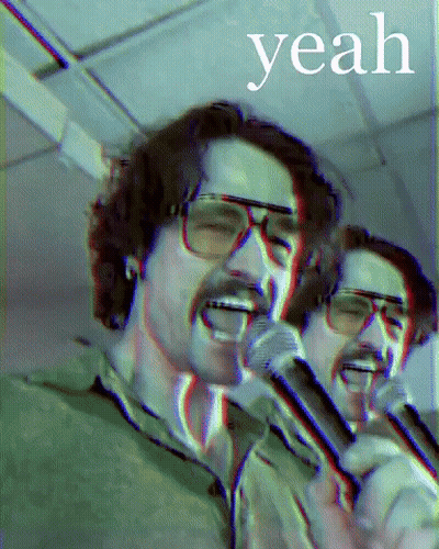 A Man With Glasses Singing Into A Microphone With The Word Yeah Behind Him GIF