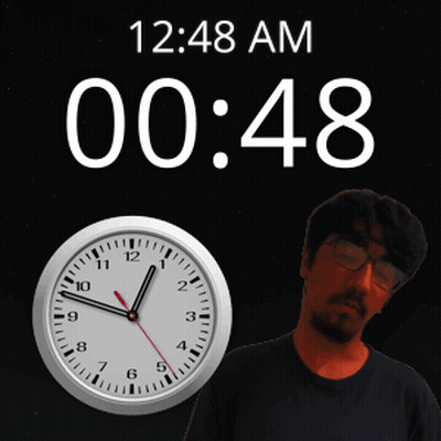 A Man With Glasses Stands In Front Of A Clock That Reads 1:48 Am GIF