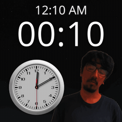 A Man With Glasses Stands In Front Of A Clock That Reads 12:10 Am GIF