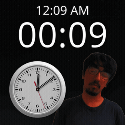 A Man With Glasses Stands In Front Of A Clock That Says 12:09 Am GIF