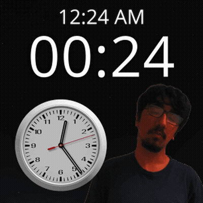 A Man With Glasses Stands In Front Of A Clock That Says 12:24 Am GIF