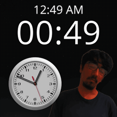A Man With Glasses Stands In Front Of A Clock That Says 12:49 Am GIF