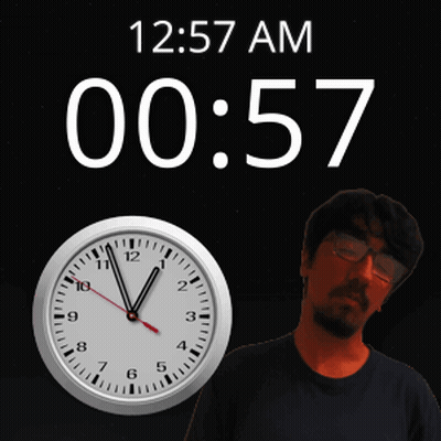 A Man With Glasses Stands In Front Of A Clock That Says 12:57 Am GIF
