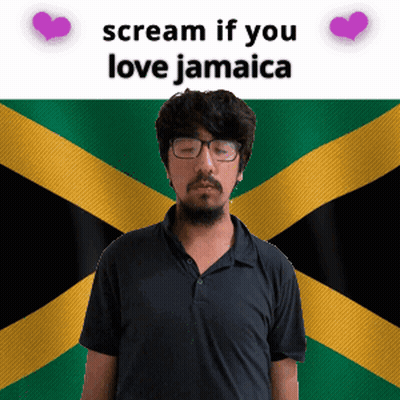 A Man With Glasses Stands In Front Of A Jamaican Flag GIF