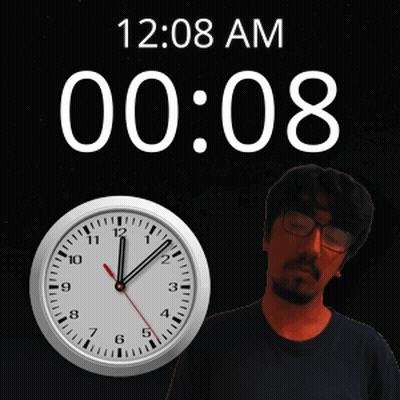 A Man With Glasses Stands Next To A Clock That Says 12:08 Am GIF