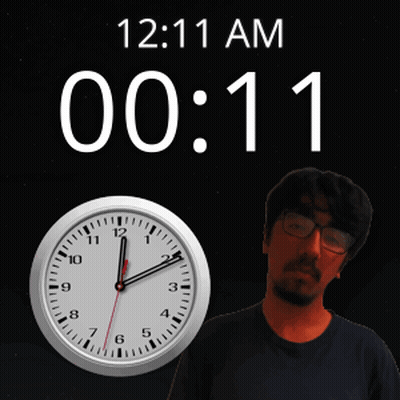 A Man With Glasses Stands Next To A Clock That Says 12:11 Am GIF