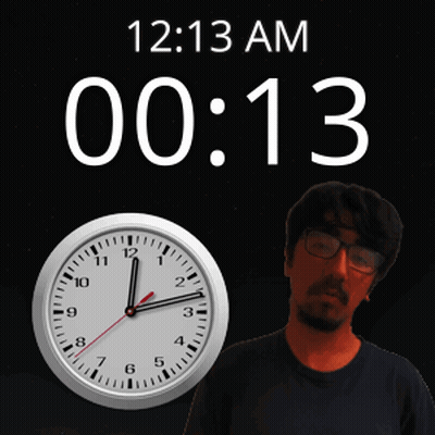 A Man With Glasses Stands Next To A Clock That Says 12:13 Am GIF