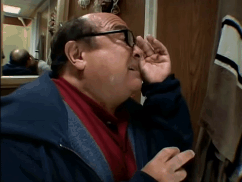 A Man With Glasses Wipes His Nose With His Hand In Front Of A Mirror GIF