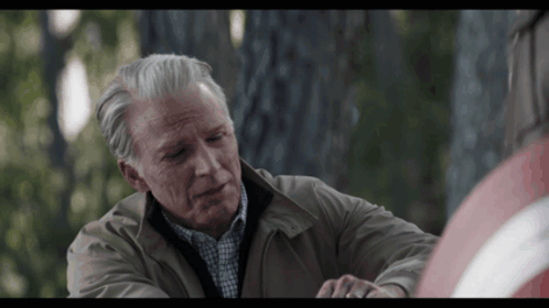 A Man With Gray Hair And A Brown Jacket Is Sitting Next To A Woman GIF