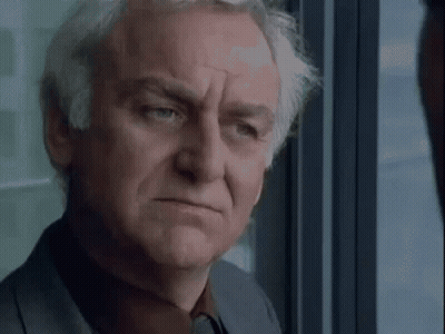 A Man With Gray Hair Is Looking Out Of A Window . GIF