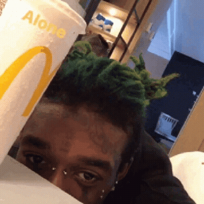 A Man With Green Hair Is Peeking Out From Behind A Mcdonalds Cup That Says Alone GIF