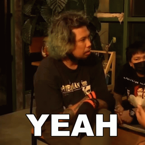 A Man With Green Hair Is Sitting At A Table With The Word Yeah Above Him GIF