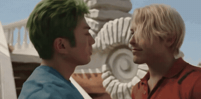 A Man With Green Hair Kisses Another Man In Front Of A Statue GIF