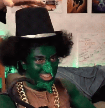A Man With Green Paint On His Face Is Wearing A Top Hat And A Gold Chain . GIF