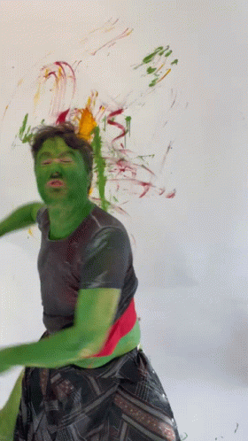 A Man With Green Paint On His Face Stands In Front Of A White Wall GIF